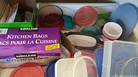 Kitchen bags box, plastic containers and lids, disposable cups visible inside a white plastic bin