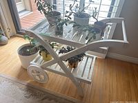 Side view of white plastic two-tier serving cart with items on shelves, showing wheels and curved supports.