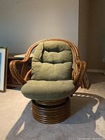 Front view of rattan swivel chair showing rounded backrest and green cushion seat and backrest.