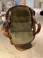 Front view of rattan swivel chair showing olive-green tufted cushion and curved rattan arms.