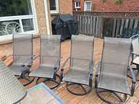 Four cast aluminum swivel chairs with mesh seats and backs arranged on wooden deck, showing weathering consistent with outdoor use.