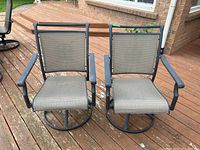 Pair of outdoor swivel chairs made of cast aluminum with grey mesh seats and backs shown side by side on a wooden deck.