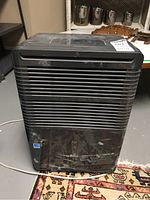 Front view of the black Danby Premiere DDR7081CP dehumidifier showing air vents and attached power cord on the ground.