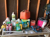 Photo showing assortment of garden supplies, Jerry cans, tools and cleaning products arranged on a wooden shelf in a garage or shed.