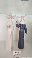 Front view of two Lladro nun figurines placed side by side on a white surface.