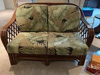 Front view of rattan love seat with leaf pattern cushions showing two seat cushions and two back cushions