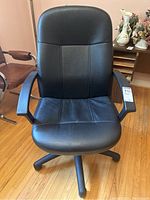 Front view of black vinyl upholstered office desk chair with molded frame sitting on hardwood floor.