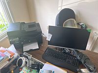 HP printer, monitor, keyboard on desk with various cables and power cords, near window.