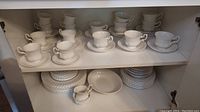 Full set including teacups on top shelf and stacked plates and bowls on bottom shelf.