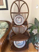Front view of rattan corner shelving unit with decorative curved top and three visible triangular shelves.