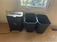 View of the Royal PX1201 shredder and two black plastic waste bins placed side by side on carpet near window.