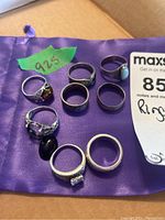 Eight silver rings laid out on purple pouch with 925 label, showing variety of designs and gemstones including amber, turquoise and black onyx.