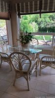 Full view of the rattan table with glass top and surrounding four rattan chairs with cushions in sunroom.
