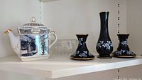 James Sadler teapot with transfer images alongside three black Prinknash pottery pieces and clear glass bowl.