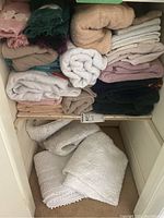 Stacked towels in multiple colors, including beige, white, pink, green, and dark colors, folded on a shelf.