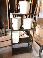Full view of the metal utility shelving unit with white buckets placed on shelves but not included in sale.