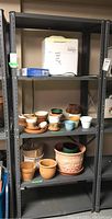 Front view of shelving unit loaded with various pots and small appliances, showing condition and shelving surface.