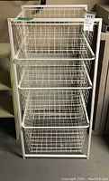 Front view of white coated metal wire shelving unit with four basket drawers, showing overall structure and condition.