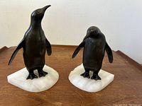 Pair of bronzed metal penguin bookends on white marble bases.