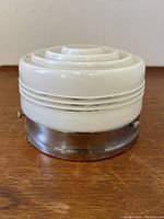 Side view of the circular ribbed opaque glass ceiling lamp fixture on a wooden surface showing metal base.