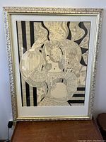 Full front view of the framed silkscreen print of nude fantasy scene in silver decorative frame on wood surface.