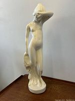 Front view of the large white ceramic nude female figurine statue, showing figure covering part of her face with right arm and holding draped cloth with left hand.