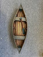 Top-down view of the wooden canoe display piece showing slatted wood interior and paddle inside.