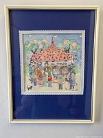 Frontal view of the framed watercolour painting showing festive crowd around a carousel, with white frame and blue matting.