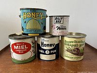 Front view of all five vintage honey advertising tins grouped showing designs and size variety.