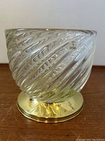 Side view of the clear Murano glass ice bucket showing the swirling texture and brass base with designer stickers attached.