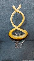 Front view of the 12-inch tall abstract art glass sculpture with amber intertwined loops and clear base with small nick.