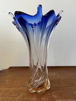 Frontal image of the vintage Murano art glass vase placed on a wooden surface showing its flared wave form edges with blue and pink coloring.