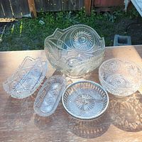 Top-down photo of all five glass pieces on a wooden table outdoors, showing intricate cut glass patterns and clear transparency.