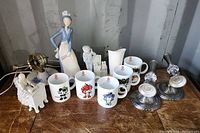 Overview of the lot showing the Beijing Olympic coffee mugs, porcelain figurines, vintage lamp, and candle holders