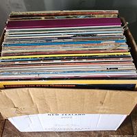 Photo looking down into a cardboard box full of various LP record sleeves showing many colorful album covers stacked vertically.