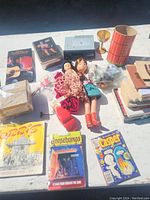 Overview of lot showing dolls, books, comics, cassette tapes, tape deck and some trinkets spread on table.