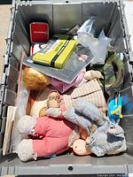 Metal storage bin containing various items including dolls, books, toys, and collectibles, all weathered.