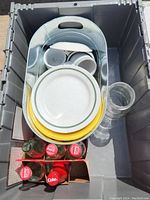 Overhead view of glassware and drinkware tightly packed in plastic bin including metal bin, plates, glasses, and four Coca-Cola glass bottles in a cardboard carrier.