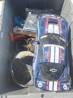 Photo of large blue Chevrolet Corvette toy race car, silver metal object, and other items inside a grey storage bin.
