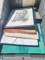 Grey plastic bin containing a stack of various vintage papers including comic books and magazines with a framed portrait on top.