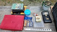 Photo showing assorted books, punch set box, tins, glassware, jigger, and other various small items.