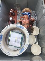 Storage bin open showing assorted glassware, ceramic items, and doll
