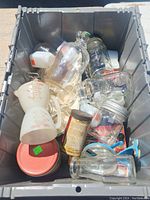 Top-down photo showing vintage jars, measuring containers, glass bottles, and an old tin inside a gray storage bin.