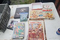 Overview of comic books, magazines, board game, marbles in bag, and some additional paper items on white table.