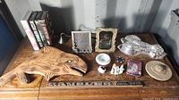 Photo of wooden carved fish wall hanging, picture frames, small trinkets and decorative plaque on table