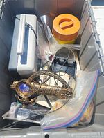 Photo showing an assortment of items including a decorative brass telescope/binoculars, a metal handle box, a plastic container, various plastic bags with small parts, and a small black electric device.