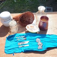 Overview photo showing all items in the lot including glass jars, wicker basket, small ceramic pot, white ceramic serving dish, silverware in a blue pouch
