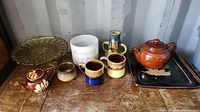 Side angle of lot showing teapot, mugs, glass plate, and other pottery items on wooden surface