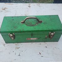 Closed green metal Sears Craftsman toolbox showing top handle and lock mechanism, surface rust and dirt present.
