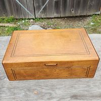 Closed wooden box with decorative inlay lines and small handle on the front.